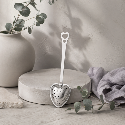 Heart Shaped Tea Infuser – authentic silver heart-shaped metal tea infuser displayed in the Carpe Diem Dream Botanical Studio with Roman Clay textures, cool greige wood, matte ceramics, eucalyptus, mauve linen, natural stone styling, and cool diffused daylight. — for Carpe Diem Dream