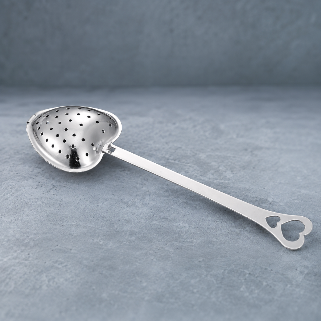 Heart Shaped Tea Infuser – authentic silver heart-shaped metal tea infuser photographed on a cool blue-gray stone surface with a softly textured blue-gray backdrop, soft contact shadows, crisp product detail, and premium editorial studio styling. — for Carpe Diem Dream