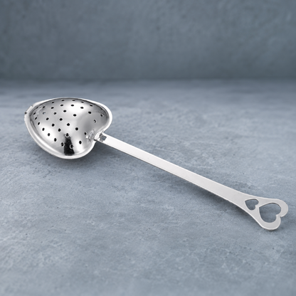 Heart Shaped Tea Infuser – authentic silver heart-shaped metal tea infuser photographed on a cool blue-gray stone surface with a softly textured blue-gray backdrop, soft contact shadows, crisp product detail, and premium editorial studio styling. — for Carpe Diem Dream