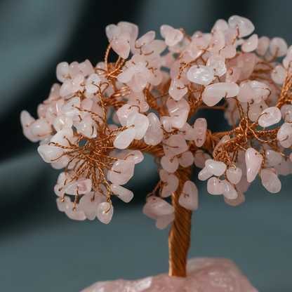Close-up of Rose Quartz crystal tree with polished tumbled stones and copper wire branches against a muted teal backdrop. — for Carpe Diem Dream