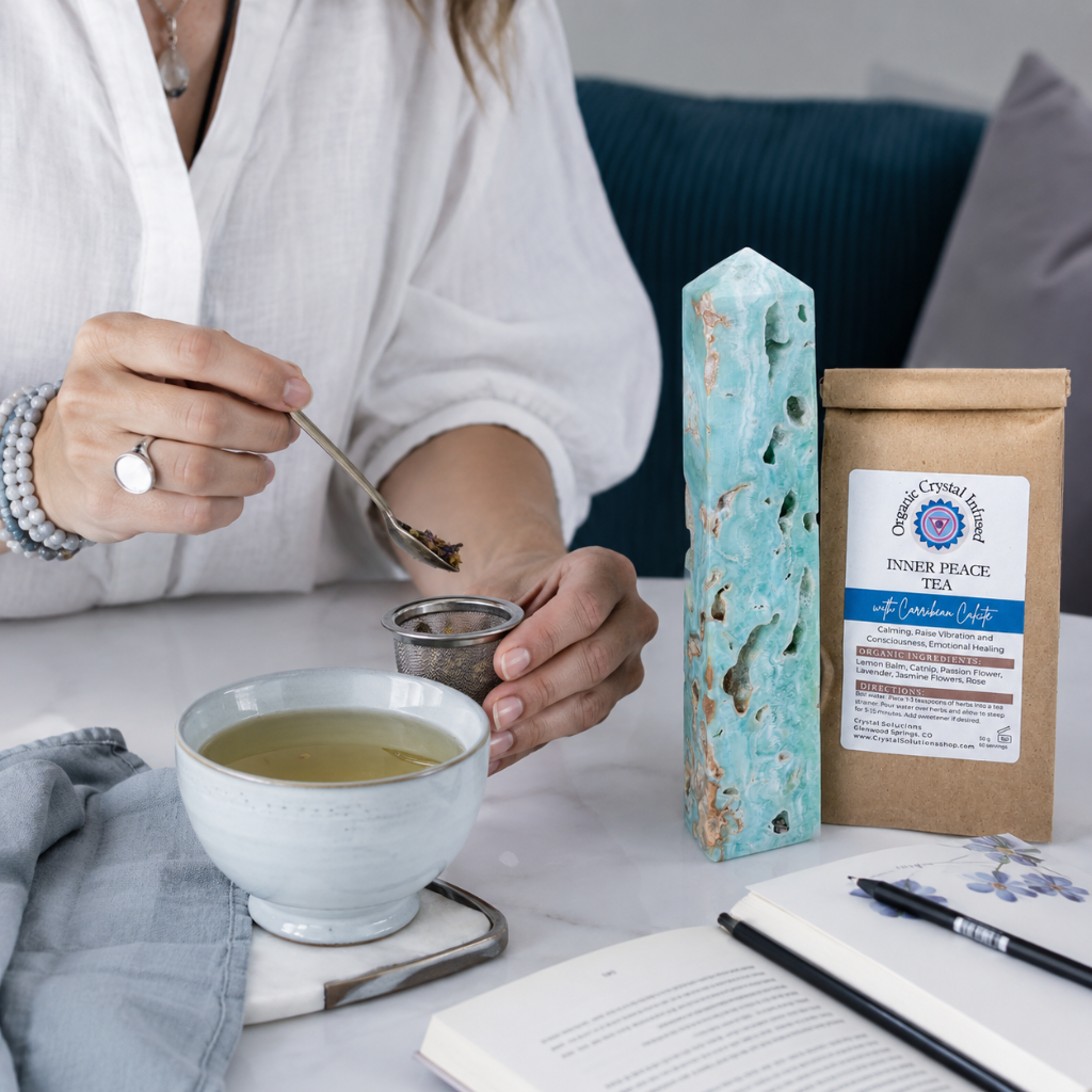 Inner Peace Tea – Organic Crystal-Infused Herbal Tea with Carribean Calcite shown in an authentic tea preparation moment with loose herbs being added to a stainless tea strainer, clear tea, soft blue textiles, natural stone, and cool diffused daylight. The product supports a calm, intentional ritual for reflection and inner peace. — for Carpe Diem Dream