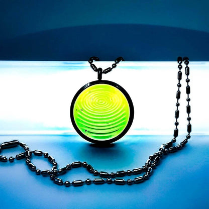 A clear jade ion glass defense pendant with a spiral design on a dark metal chain, displayed on a blue background. — for Carpe Diem Dream