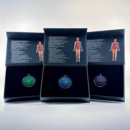 Three ion glass defense pendants in green, blue, and red displayed inside open presentation boxes with printed inserts on a white background. — for Carpe Diem Dream