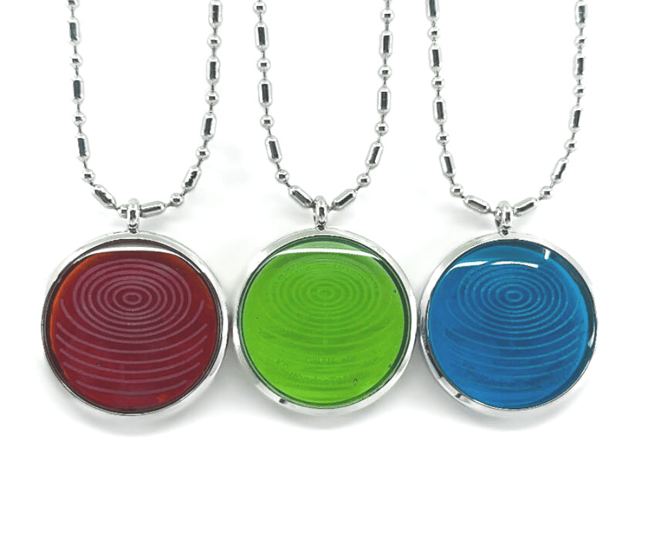 Three ion glass defense pendants with spiral designs in red, green, and blue, displayed side by side on silver chains against a white background. — for Carpe Diem Dream
