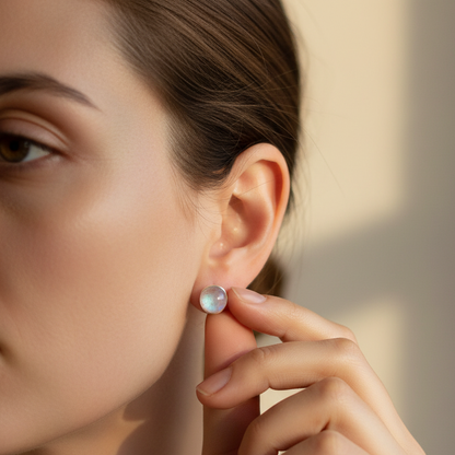 Woman’s hand adjusting a silver labradorite stud earring against warm indoor lighting. — for Carpe Diem Dream