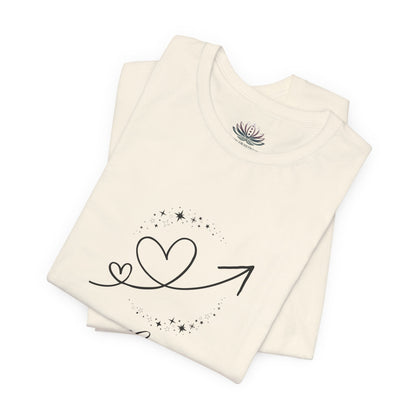 Leo Rising I Shine zodiac T-shirt in Natural with black celestial heart and arrow artwork, shown folded in a supplier mockup. — for Carpe Diem Dream