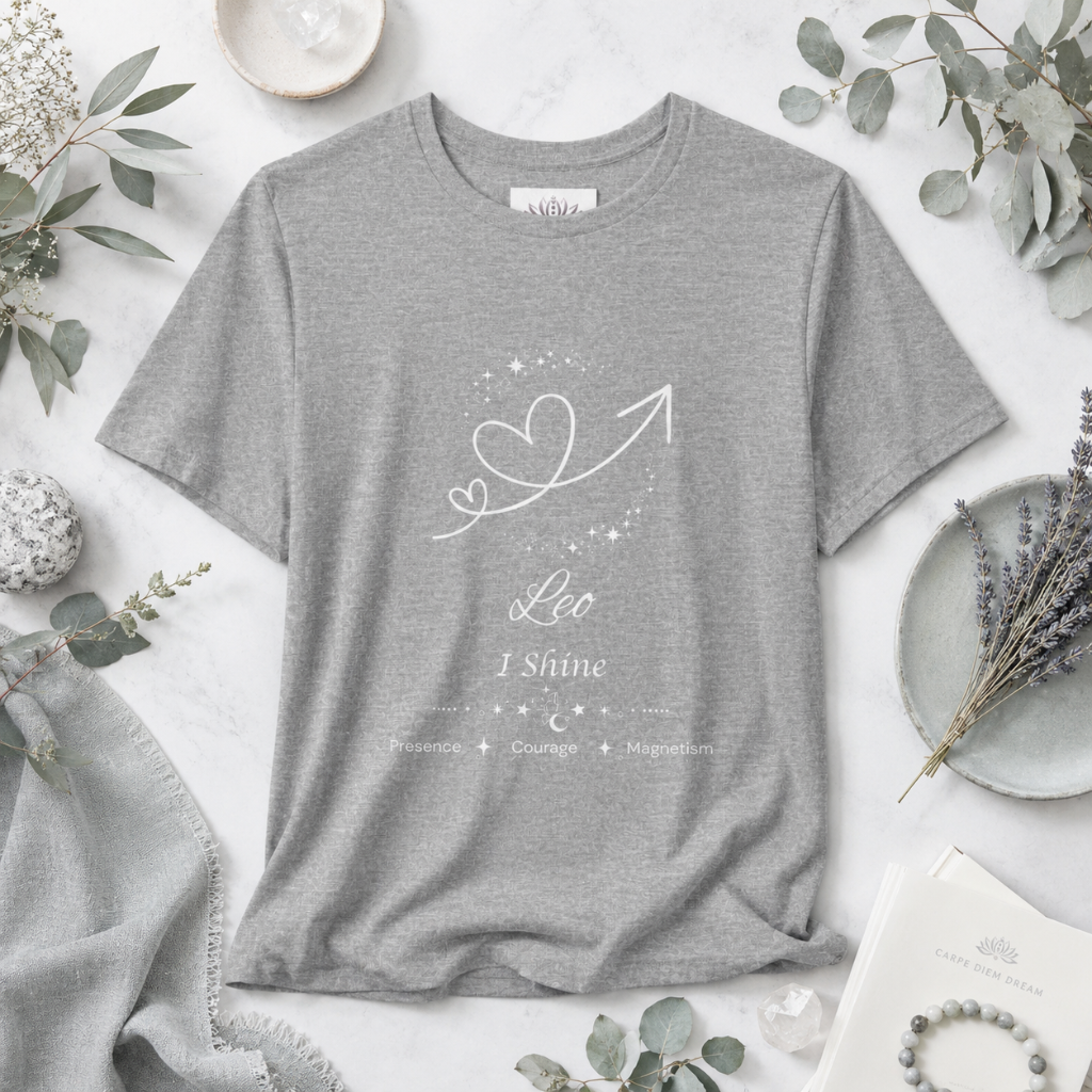 Leo Rising I Shine zodiac T-shirt in Athletic Heather with white celestial heart and arrow artwork and Presence, Courage, Magnetism text, styled in a cool-toned studio botanical flat lay. — for Carpe Diem Dream