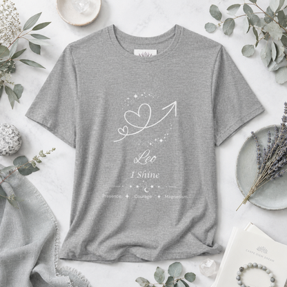 Leo Rising I Shine zodiac T-shirt in Athletic Heather with white celestial heart and arrow artwork and Presence, Courage, Magnetism text, styled in a cool-toned studio botanical flat lay. — for Carpe Diem Dream