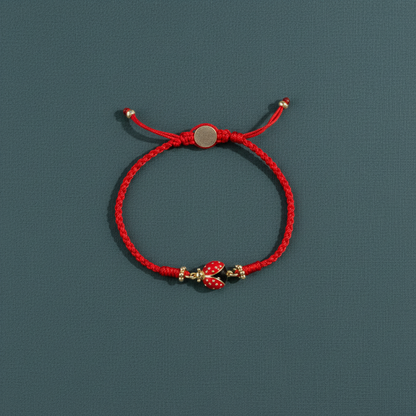 A red string bracelet with a gold-plated ladybug charm displayed on a muted teal surface in soft natural light. — for Carpe Diem Dream