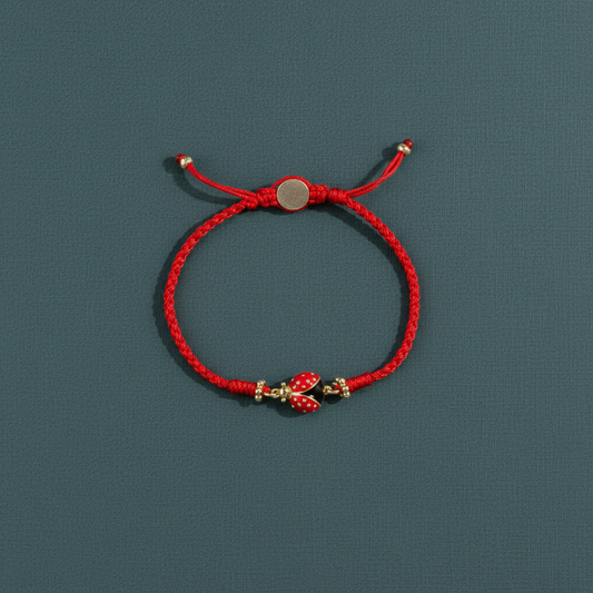 A red string bracelet with a gold-plated ladybug charm displayed on a muted teal surface in soft natural light. — for Carpe Diem Dream