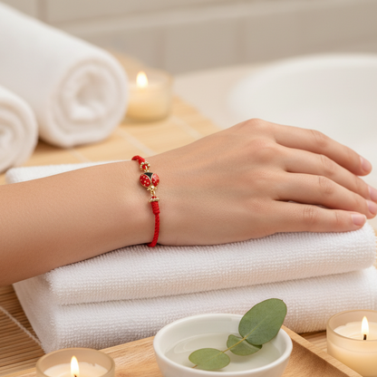 A red string bracelet with a gold-plated ladybug charm shown on a relaxed wrist resting atop folded white spa towels beside lit candles, eucalyptus leaves, and a warm serene backdrop. — for Carpe Diem Dream
