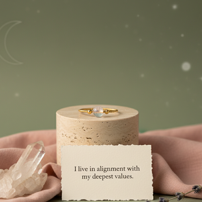Gold moonstone ring displayed on travertine pedestal with affirmation card and clear quartz cluster against soft sage backdrop. — for Carpe Diem Dream