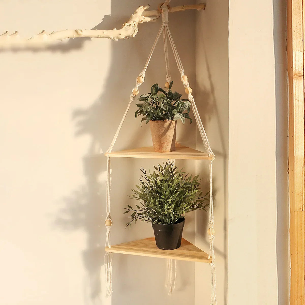 A two-tier macrame corner wall shelf with wooden tiers is styled with potted plants and displayed against a softly lit neutral wall. — for Carpe Diem Dream