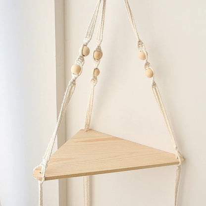 A close-up view of a macrame corner wall shelf showing knotted rope details and a natural wood triangular shelf against a light neutral wall. — for Carpe Diem Dream