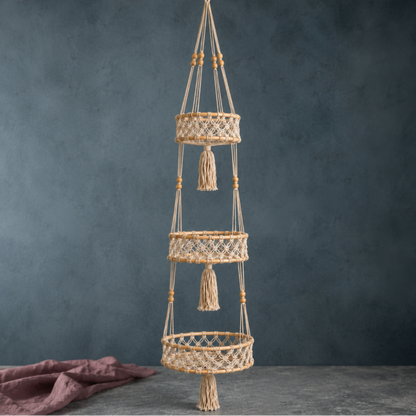 Triple-tier macrame hanging wall basket professionally photographed with rattan rings, cotton cord, and mauve linen on a cool blue-gray studio backdrop. — for Carpe Diem Dream
