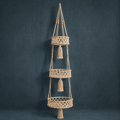 Triple-tier macrame hanging wall basket with rattan rings and cotton cord on a dark teal linen backdrop. — for Carpe Diem Dream