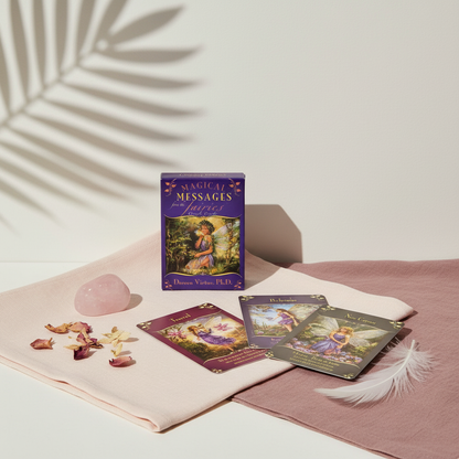 A Magical Messages From The Fairies Oracle deck displayed with several colorful cards on draped blush fabric alongside a rose quartz crystal, petals, and a feather with soft botanical shadow in the background. — for Carpe Diem Dream