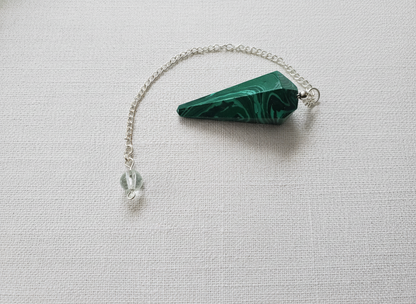 Malachite crystal pendulum with silver chain resting on a textured white surface, showcasing deep green swirls and natural patterning – for Carpe Diem Dream.