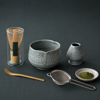 Matcha Ritual Set featuring a bamboo whisk, ceramic tea bowl, whisk holder, scoop, strainer, and matcha accessories arranged on #374F59 textured linen with soft shadows and cool diffused lighting. — for Carpe Diem Dream