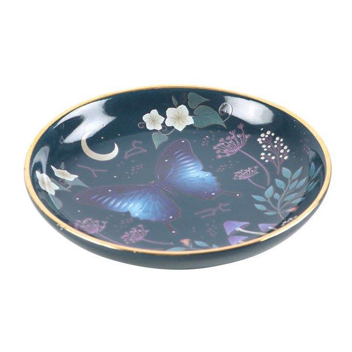 Angled view of the Midnight Moth Celestial Trinket Dish showcasing a blue night sky design with a moth, moon, and floral details, finished with gold edging, styled for Carpe Diem Dream.
