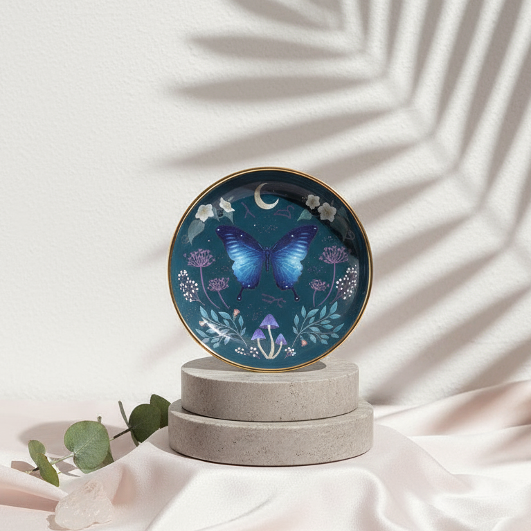 Midnight Moth Celestial Trinket Dish with gold edge displayed on gray travertine cylinders over blush silk fabric, illuminated by soft daylight shadows, styled by Carpe Diem Dream.