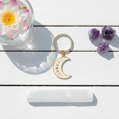 Moon Phase Celestial Keychain styled in a serene outdoor flatlay on a white wooden deck beside a crystal bowl with a lotus flower, selenite wand, and amethyst crystals, captured in natural sunlight for Carpe Diem Dream.