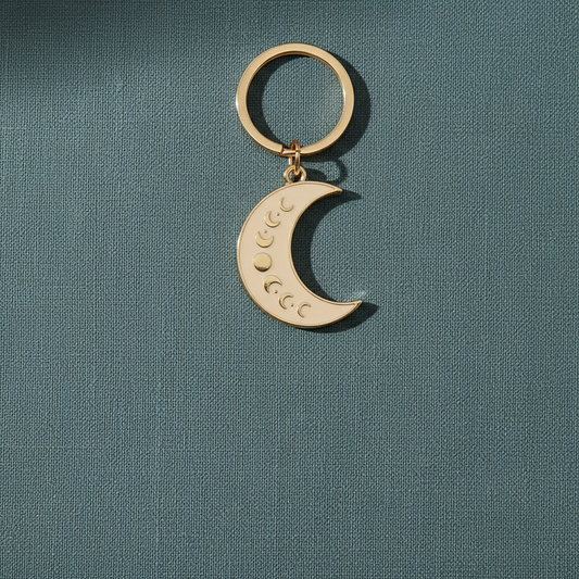 Gold moon phase keychain displayed on a soft teal textured background – for Carpe Diem Dream.