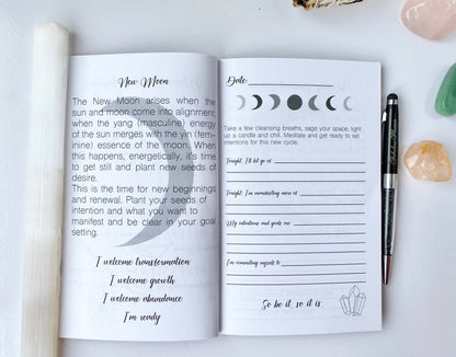 Interior spread of Moon Rituals & Manifestation Journal showing New Moon intention setting page with lunar phase graphics, guided prompts, and lined writing sections beside a pen on a white background — for Carpe Diem Dream