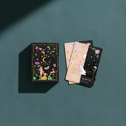 A Moon Witch Oracle deck box with floral celestial artwork displayed beside a spread of illustrated oracle cards on a textured deep teal linen surface with soft directional lighting. — for Carpe Diem Dream