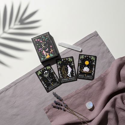 A Moon Witch Oracle deck displayed with several illustrated cards, a selenite wand, and a small crystal arranged on draped mauve fabric against a soft neutral background with botanical shadow. — for Carpe Diem Dream