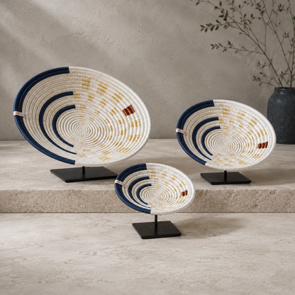 Moonrise Wall Basket small, medium, and large handwoven decorative wall baskets displayed together on black stands, showing shallow bowl shape and natural, navy, and golden woven patterns. — for Carpe Diem Dream