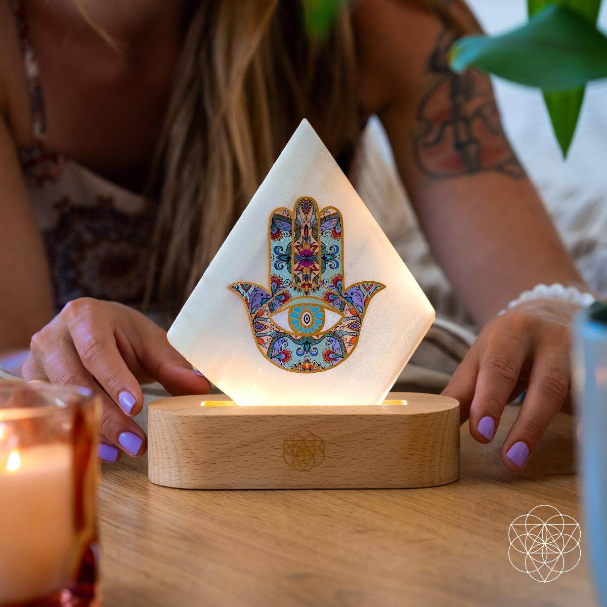 Selenite Hamsa lamp on a wooden base surrounded by candles and crystals, symbolizing calm energy and protection-styled for Carpe Diem Dream.