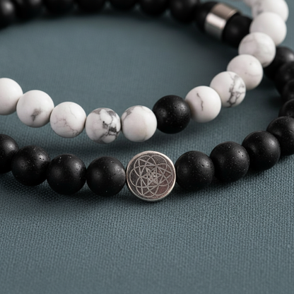 A close-up view of black and white gemstone beads with a silver mandala charm resting on a muted teal textured surface. — for Carpe Diem Dream