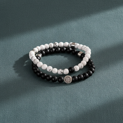 A stacked pair of black and white gemstone bracelets rests on a muted teal textured surface in soft directional light. — for Carpe Diem Dream