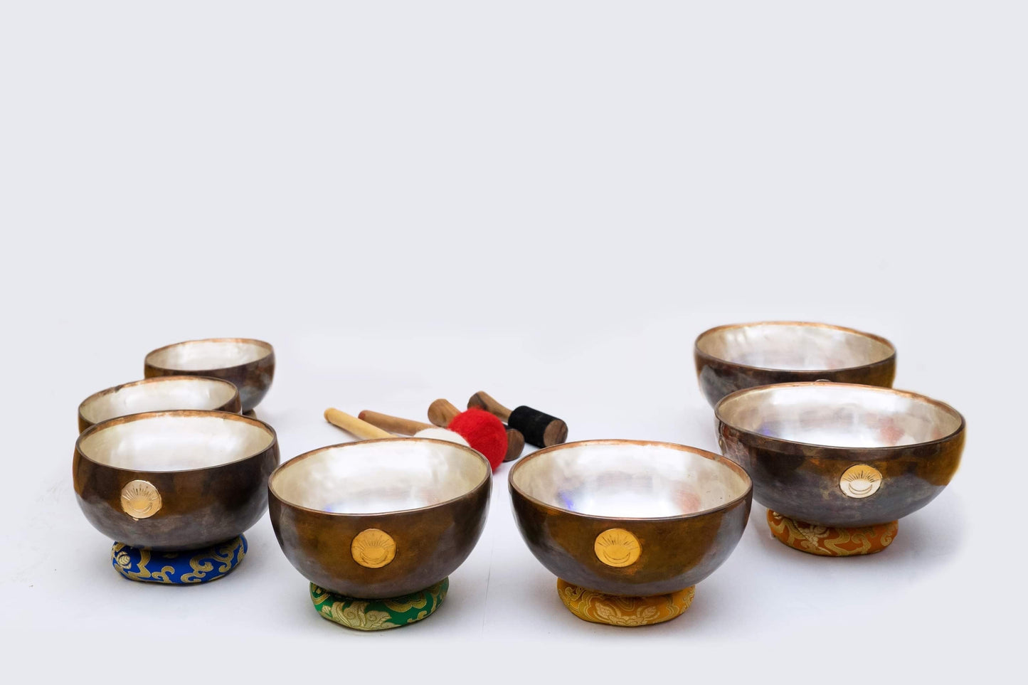 Seven chakra New Moon singing bowl set with multicolored cushions and wooden mallets displayed together on a white background. — for Carpe Diem Dream