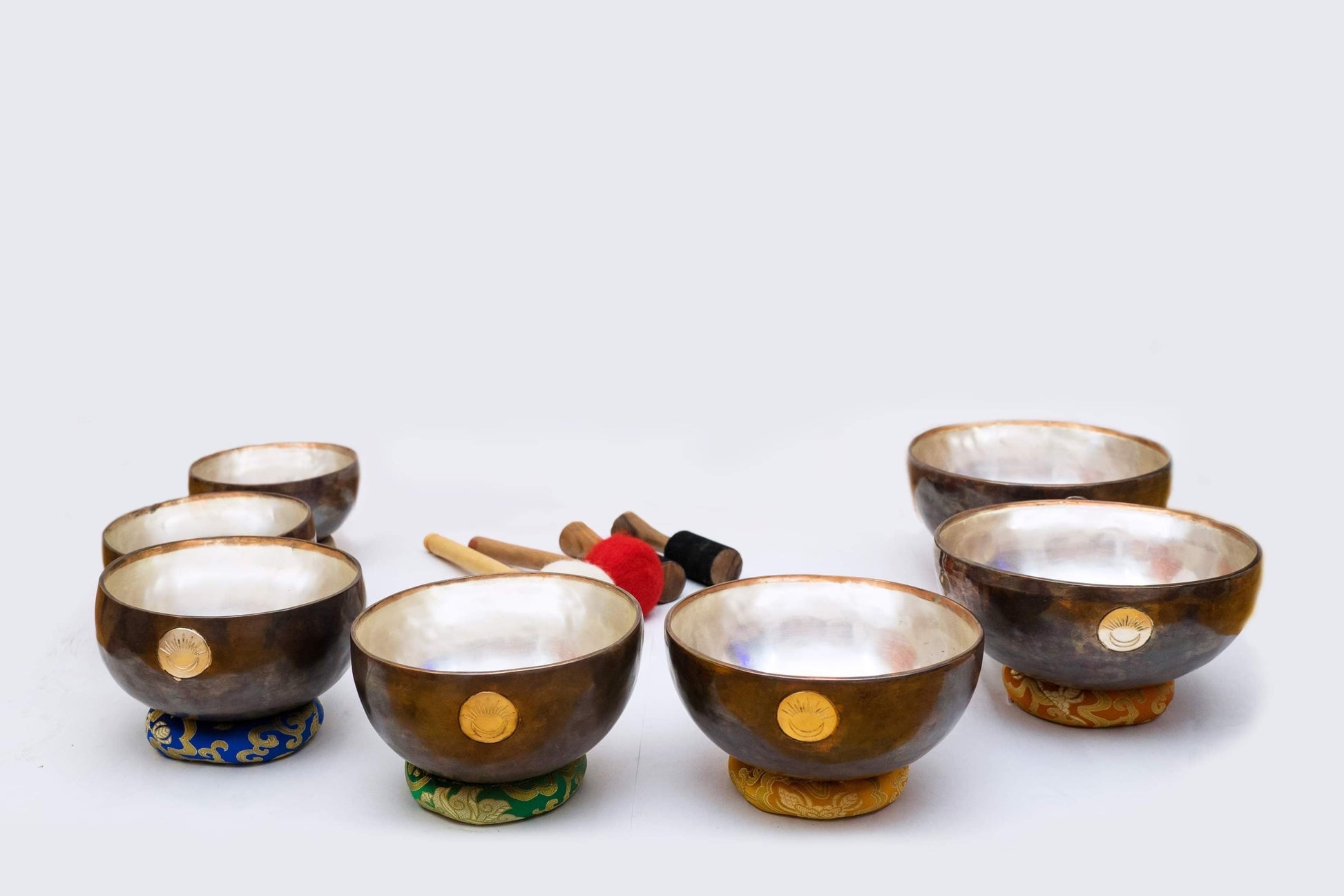 Seven chakra New Moon singing bowl set with multicolored cushions and wooden mallets displayed together on a white background. — for Carpe Diem Dream