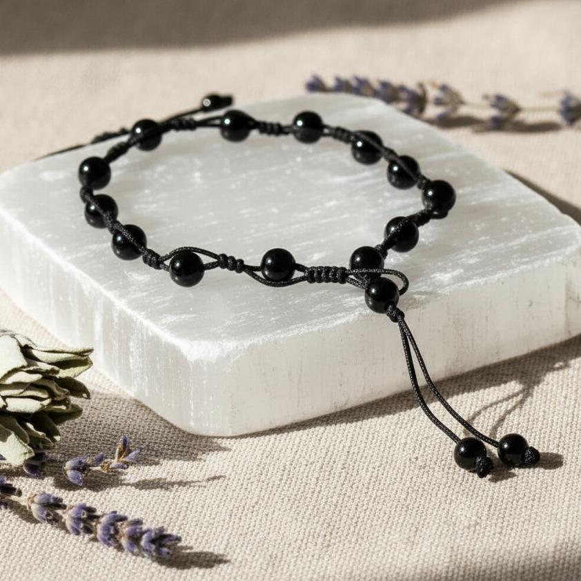 Obsidian grounding anklet displayed on a selenite slab with dried lavender and sage sprigs in soft natural light – for Carpe Diem Dream.