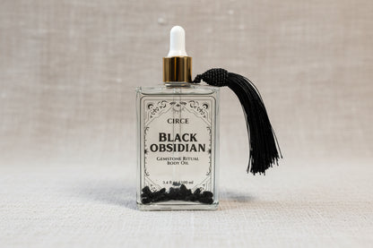 Black Obsidian Ritual Body Oil glass dropper bottle with black tassel displayed on a soft linen background. — for Carpe Diem Dream