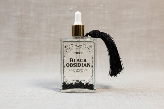 Black Obsidian Ritual Body Oil glass dropper bottle with black tassel displayed on a soft linen background. — for Carpe Diem Dream