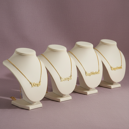 Old English Zodiac Necklace set featuring gold zodiac name pendants on display stands against a mauve background — for Carpe Diem Dream.