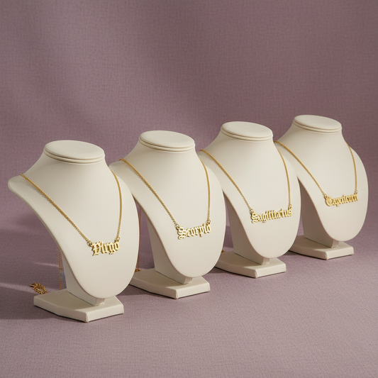 Old English Zodiac Necklace set featuring gold zodiac name pendants on display stands against a mauve background — for Carpe Diem Dream.