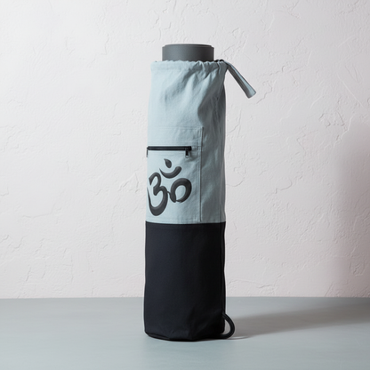 White and black Om yoga mat bag standing upright with rolled yoga mat inside against a softly lit neutral studio backdrop. — for Carpe Diem Dream