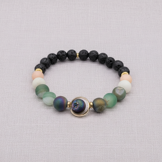 A natural stone and lava bead stretch bracelet with a round orbital focal bead and gold accents displayed on a textured linen background. — for Carpe Diem Dream