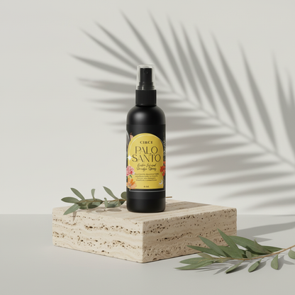 Palo Santo Smudge Spray bottle displayed on a travertine pedestal with soft botanical shadows and greenery on a neutral background. — for Carpe Diem Dream