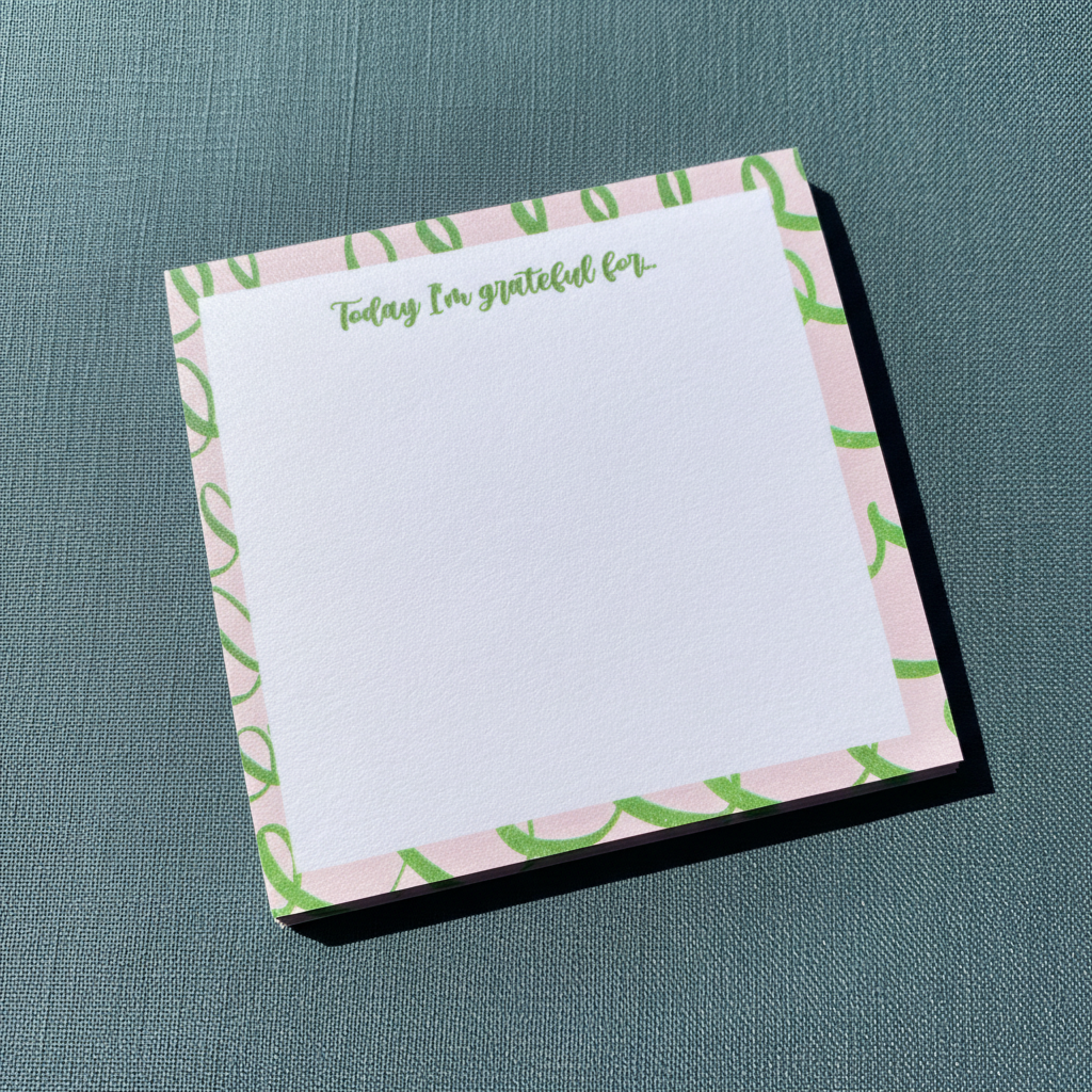 Close-up angled view of a pink and green gratitude sticky note pad with “Today I’m grateful for” text on a textured muted teal surface. — for Carpe Diem Dream
