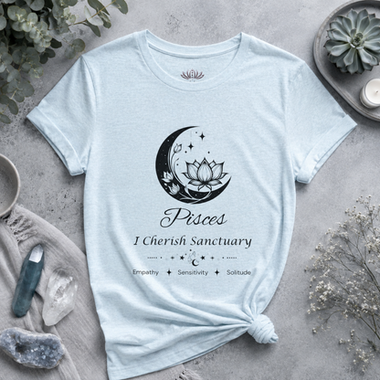 Pisces Moon I Cherish Sanctuary zodiac T-shirt in Heather Ice Blue with black moon-inspired lotus, floral, and celestial artwork and Empathy, Sensitivity, Solitude text, styled in a cool-toned studio botanical flat lay. — for Carpe Diem Dream