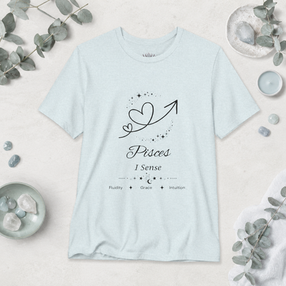 Pisces Rising I Sense zodiac T-shirt in Heather Ice Blue with black celestial heart and arrow artwork and Fluidity, Grace, Intuition text, styled in a cool-toned studio botanical flat lay. — for Carpe Diem Dream