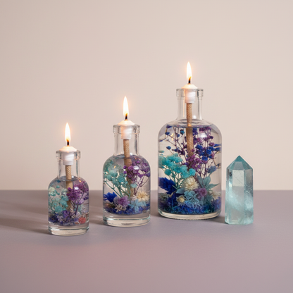 Three Pisces zodiac oil candles in different sizes with blue and purple botanicals in clear glass vessels are displayed beside a blue crystal point on a neutral surface, showing size variations. — for Carpe Diem Dream