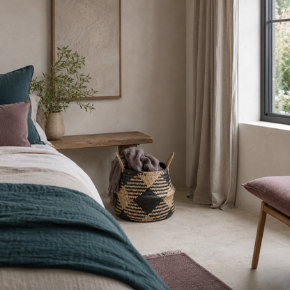 Black plaid woven storage basket styled in a calm bedroom corner with mauve textiles, dark teal bedding, and folded throw storage. — for Carpe Diem Dream