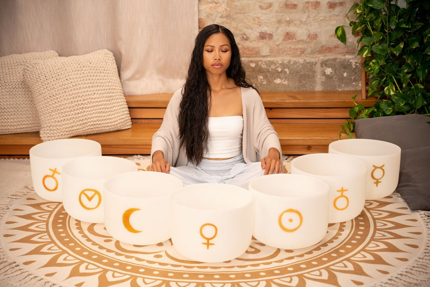 Woman seated in meditation posture surrounded by seven white frosted quartz crystal singing bowls with gold planetary symbols arranged in a circle — for Carpe Diem Dream